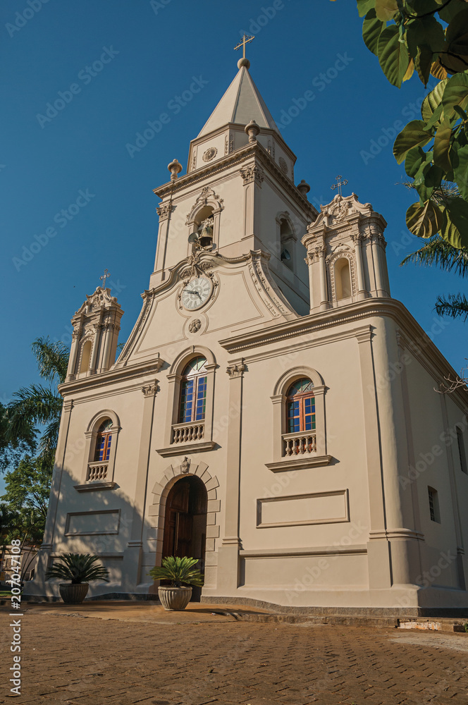 Church facade and belfry in front of a small cobblestone square with evergreen garden, in a sunny day at São Manuel. A cute little town in the countryside of São Paulo State. Southeast Brazil.