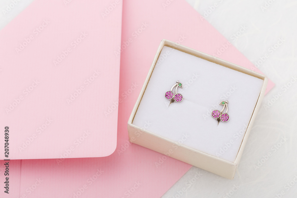 Cherry shaped earrings with crystals in gift box on pink envelope background with copy space