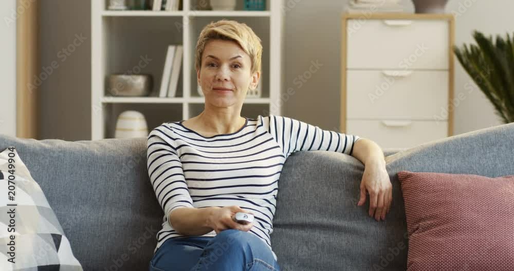 Caucasian pretty woman watching TV while sitting on the sofa at home with a remote control. Indoors Caucasian pretty woman watching TV while sitting on the sofa at home with a remote control. Indoors