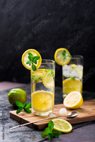 Lemon fruit lime slices caipirinha from Brazil, lemonade mint ice cubes in cold glasses on dark background, alcoholic mojito cockail ice tea green mint leaves, brown sugar spoon, copy space
