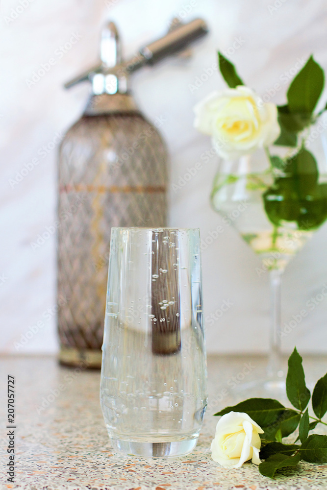 On the table is a transparent glass filled with mineral water. Still-life with white roses. On the table is a transparent glass filled with mineral water. Still-life with white roses.