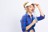Happy Lifestyle Concepts. Portrait of Upbeat Smiling Caucasian Blond Woman in Checked Shirt Drinking Blue Juice Through The Straw with Passion. Touching Sun Visor