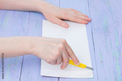 A girl cuts cardboard with a stationery knife on a purple wooden background. Close-up.