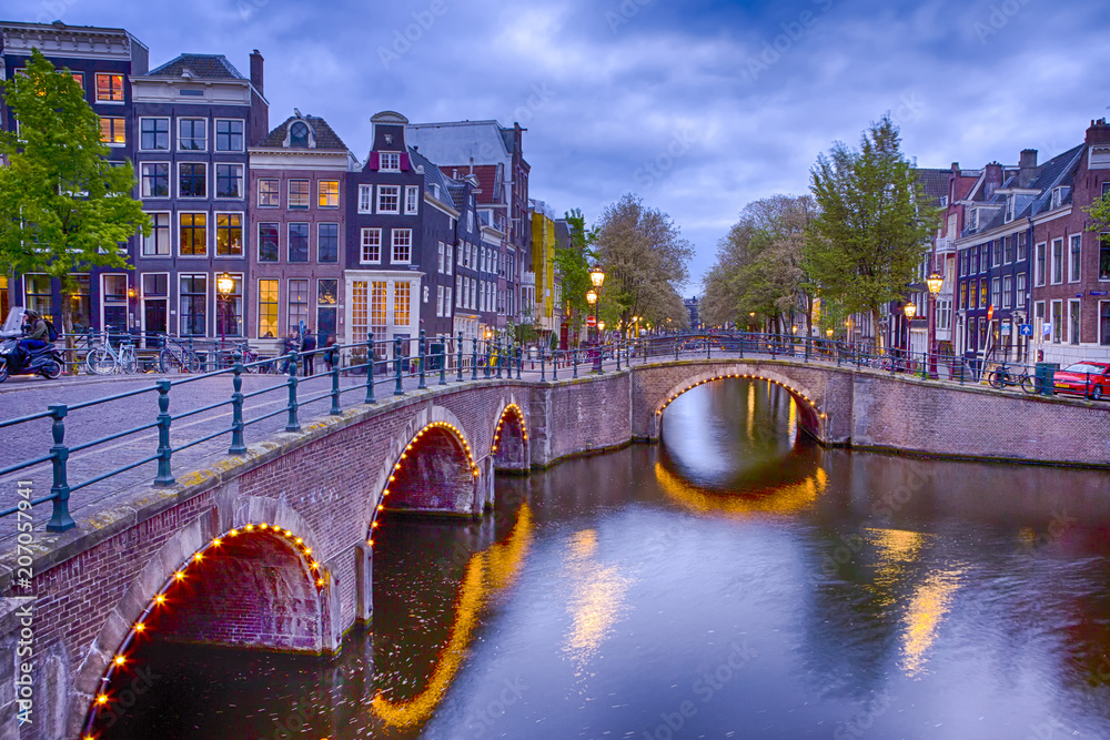 View of Amterdam Cityscape with One of Its Canals. Illuminated Bridge and Traditional Dutch Houses At Twilight.
