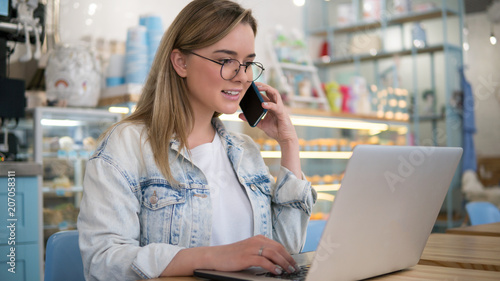 Young blonde freelance woman doing work with laptop and smartphone indoors cafe photo