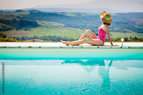 woman sitting by the pool with a cocktail  admiring green ladscape in Tuscany  Italy