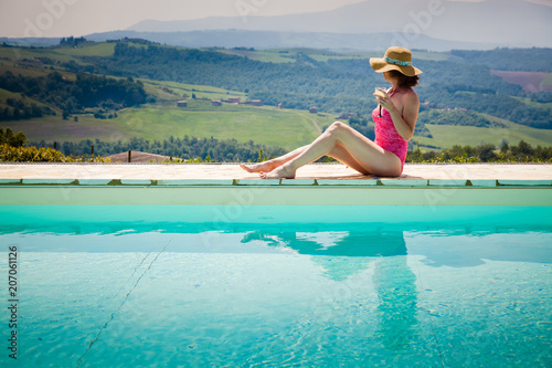 woman sitting by the pool with a cocktail admiring green ladscape in Tuscany, Italy