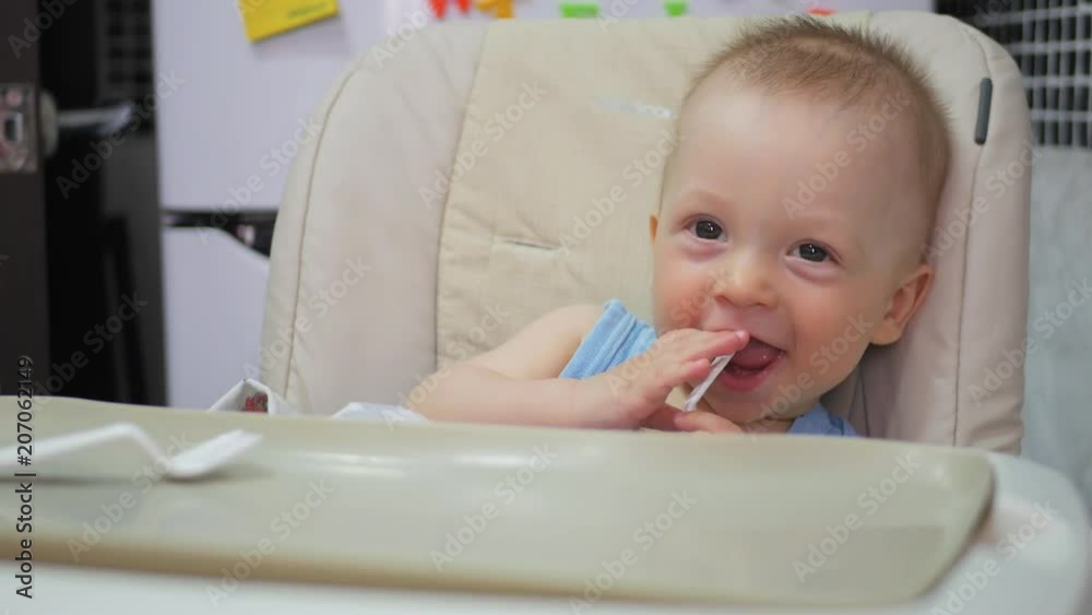 Baby sits at a children's little table. Mum feeds the child with porridge. Mother gives baby food from a spoon. Baby sits at a children's little table. Mum feeds the child with porridge. Mother gives baby food from a spoon.
