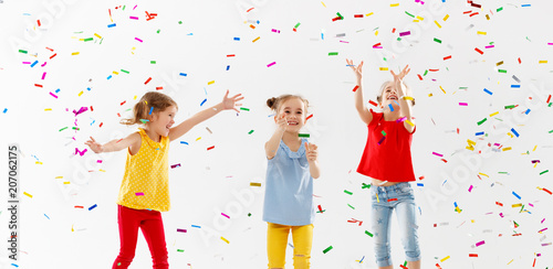 happy children on holidays jumping in multicolored confetti on white