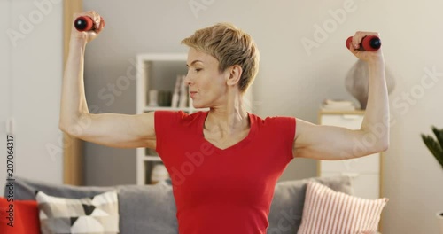 Caucasian middle aged woman swinging her hands with dumbbells at home. Indoors photo
