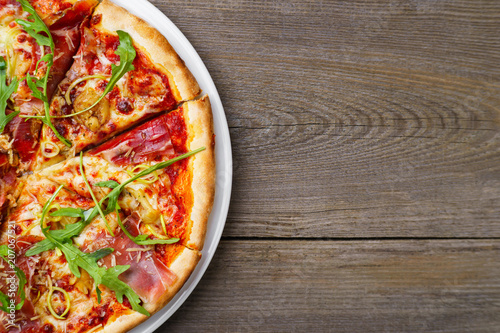 Italian traditional cuisine, pizza, food background. Fresh baked pizza with prosciutto and arugula on wooden table, copy space. Restaurant menu photo, pizzeria, food recipe, pizza delivery concept 