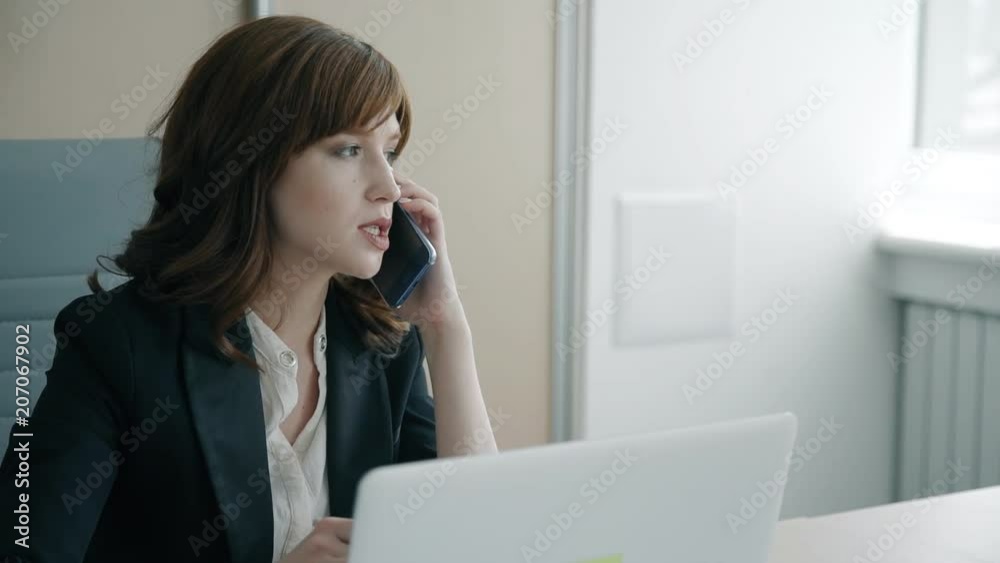 Portrait of young businesswoman talking on phone in her private office. Concept of: business people, office interior, laptop on desk, business communication, smartphone hand. Portrait of young businesswoman talking on phone in her private office. Concept of: business people, office interior, laptop on desk, business communication, smartphone hand.