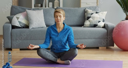 Portrait of the blond Caucasian woman resting on the yoga mat in the living room and meditating in lotos pose. Indoors photo