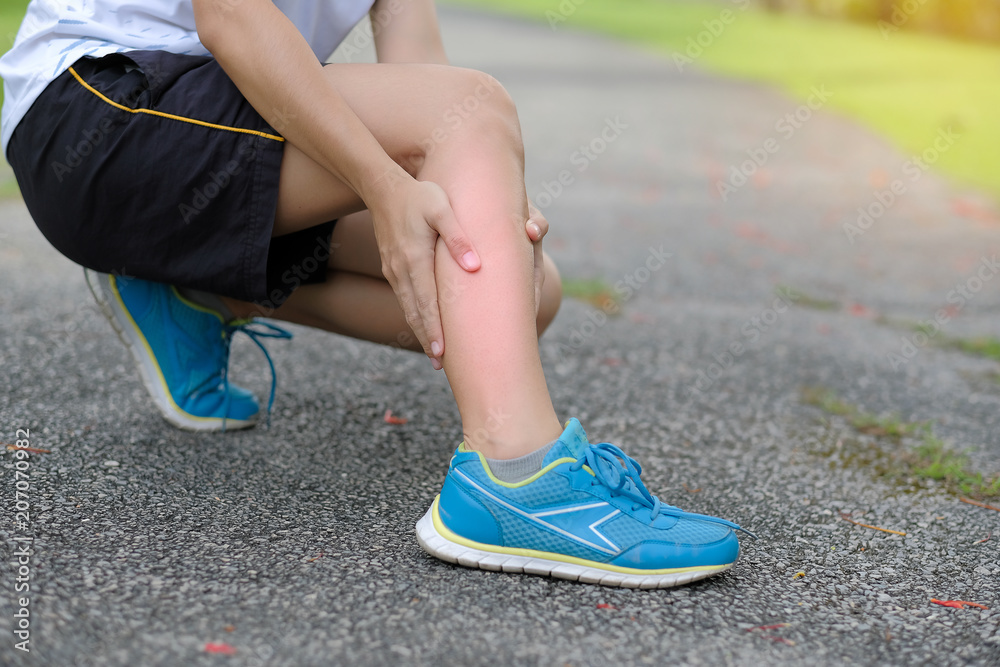 Young fitness woman holding her sports leg injury, muscle painful during training. Asian runner having calf ache and problem after running and exercise outside in summer