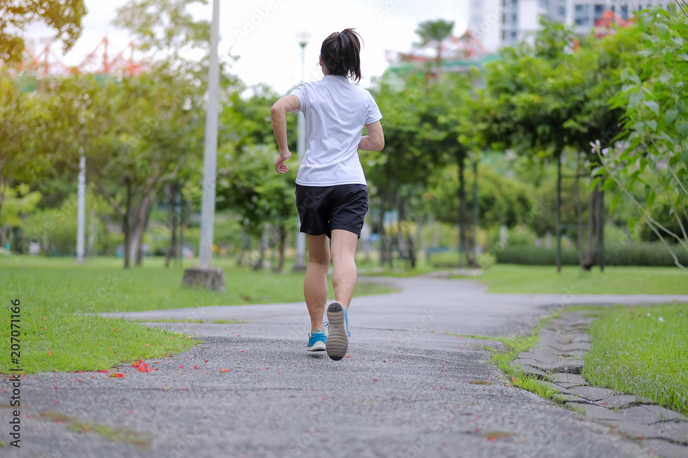 young fitness woman walking in the park outdoor, female runner running on the road outside, asian athlete jogging and exercise on footpath in sunlight morning. Sport, healthy and wellness concepts