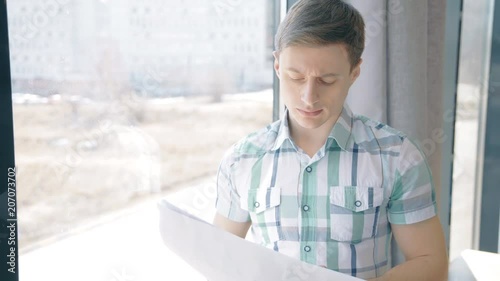 Portrait of businassman reading paper report near the window. Concept of: business people, city view, office interior, paper report.