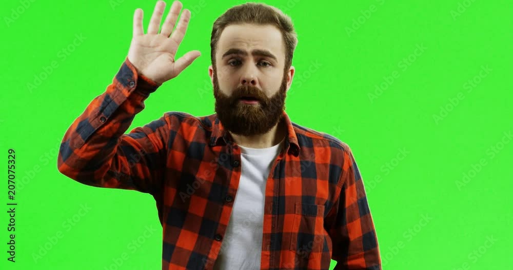 Portrait of the very shy Caucasian man with a beard and in the red motley shirt waving his hands and trying to pay attention to him while standing in front of the camera on the green screen background Portrait of the very shy Caucasian man with a beard and in the red motley shirt waving his hands and trying to pay attention to him while standing in front of the camera on the green screen background