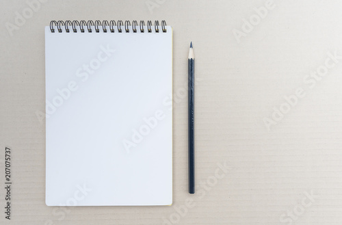Top view of open spiral blank notebook with pencil on brown background.