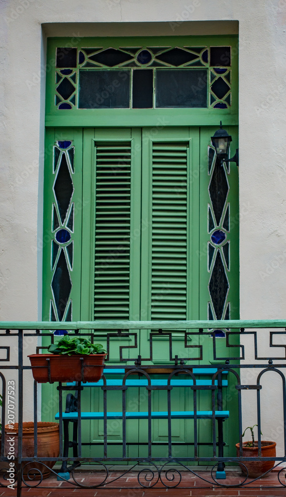 Green shuttered window on white wall with planters and green banister