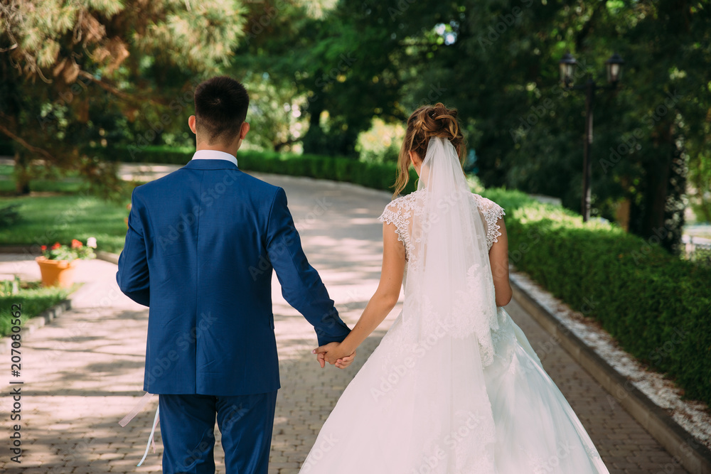 A man and a woman hold hands and walk in the park on their wedding day. Family bonds.