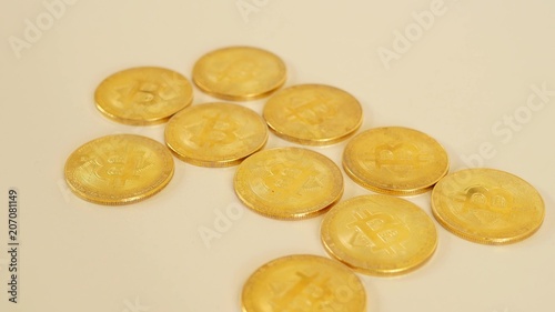 The golden coins of bitcoins lie chaotically on the table. The focus of the camera moves from the foreground to the rear.