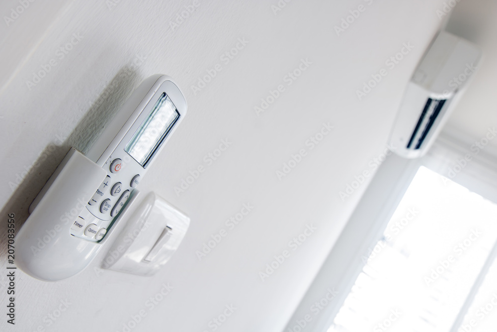 Remote control close up with air conditioner hang on white wall. Air conditioner inside the room remote controller. Remote control close up with air conditioner hang on white wall. Air conditioner inside the room remote controller.