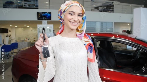 Muslim woman with car key over car show background photo