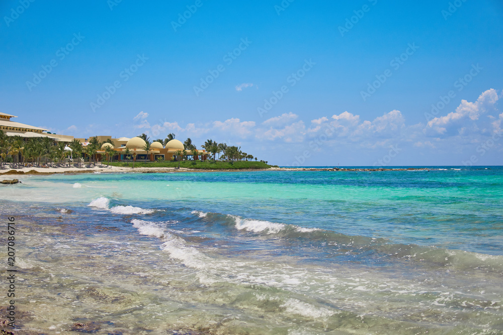 View at luxury resort hotel beach of tropical coast. Leaves of coconut palms fluttering in wind against blue sky. Turquoise water of Caribbean Sea. Riviera Maya Mexico