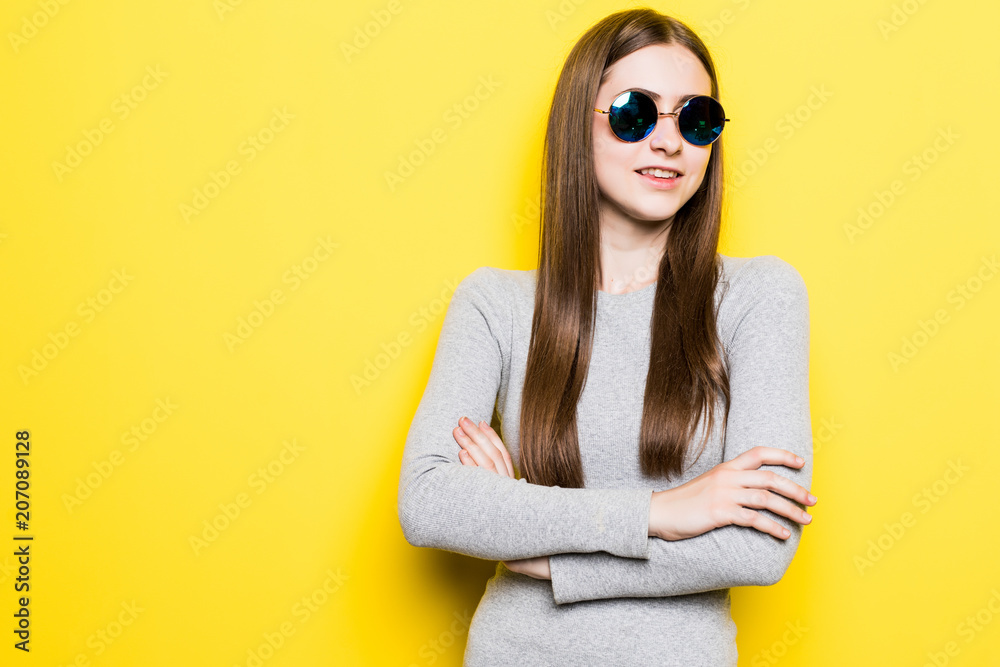 Young fashion girl with sunglasses in dress with crossed hands on yellow background Young fashion girl with sunglasses in dress with crossed hands on yellow background