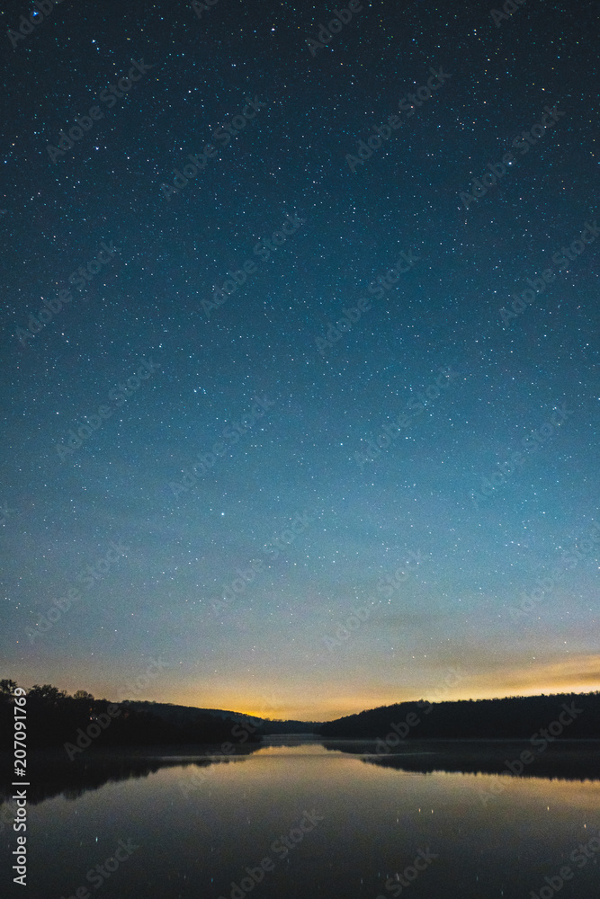 Blue dark night sky with many stars above field of trees.