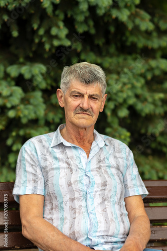An ELDERLY MAN sitting on a background of green trees