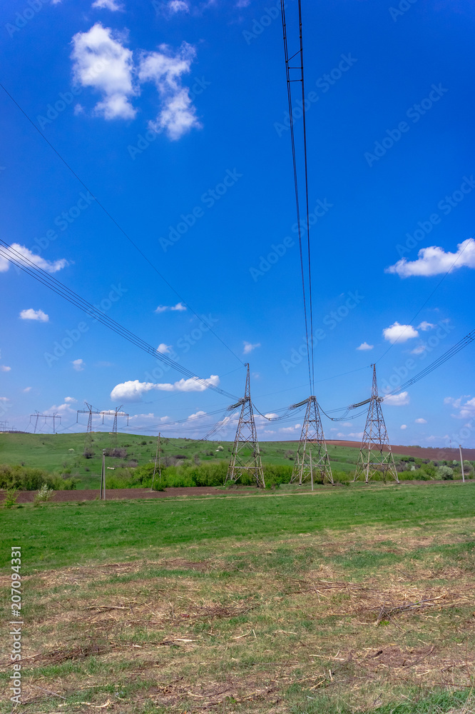 High-voltage power lines in green field against blue sky with white clouds.