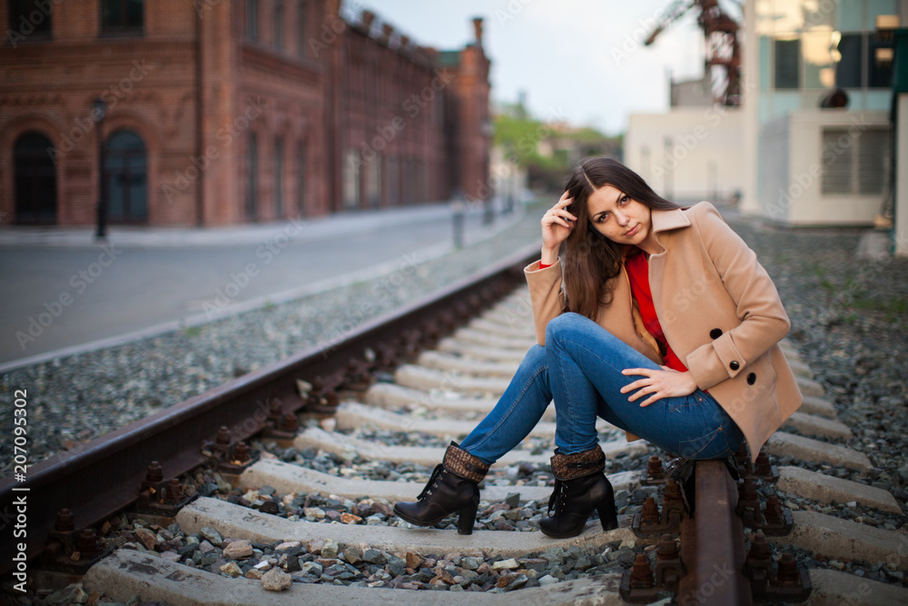 Portrait of a girl sitting on a railway in the rays of sunset. casual clothes