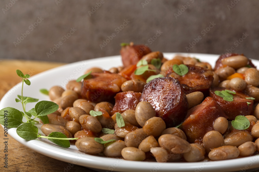 Beans with smoked pork sausages on plate and tomato sauce with green herbs Beans with smoked pork sausages on plate and tomato sauce with green herbs