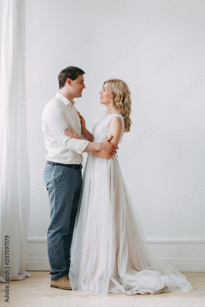 Beautiful couple in wedding photo shoot. Loft Studio in European style, bright and with large Windows. Loving people with happy faces. Bridal bouquet and stylish decorative.