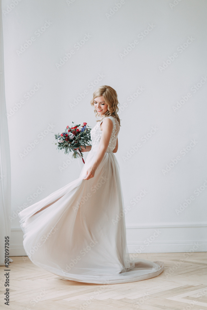 Beautiful bride in a wedding dress in a bright stylish Studio. Wedding in European style. Decor and bouquet in hand. Young girl standing, sitting and posing