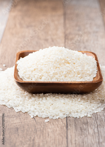 raw rice in a wooden bowl on wooden background