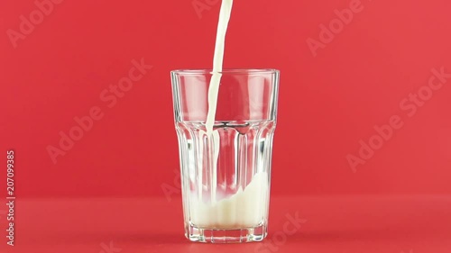 Slow motion close-up shot of cold diary milk cold beverage drink pooring into faceted glass on colored red background in studio