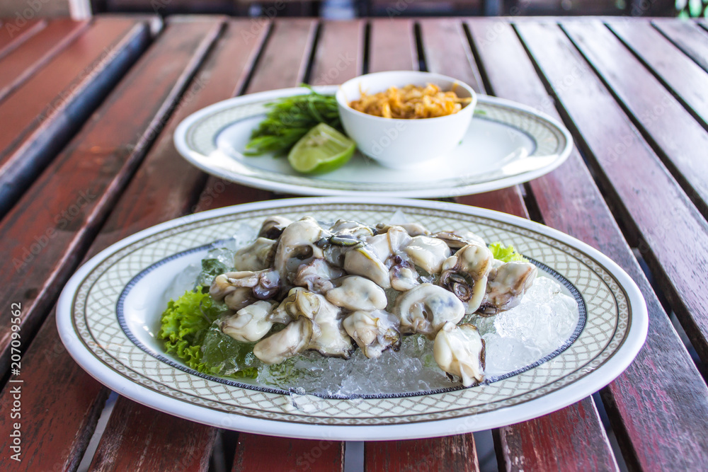 Fresh oyster shells are placed on ice cubes in a white plate on brown wood. And a dish of vegetables together. Fresh oyster shells are placed on ice cubes in a white plate on brown wood. And a dish of vegetables together.