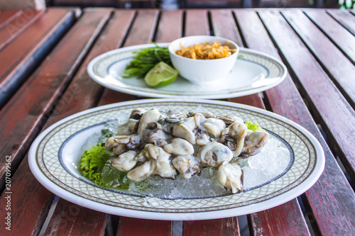 Fresh oyster shells are placed on ice cubes in a white plate on brown wood. And a dish of vegetables together.