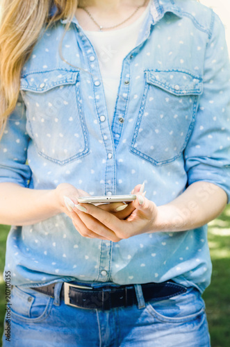 Close Up white Smartphone Mobile Cell holding in woman hands Stylish Torn Jeans Long Nails Denim Black Oled Display Nature Background