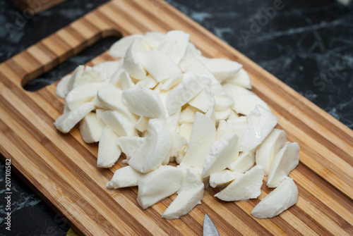 Chopped fresh mozzarella cheese with kitchen knife on wooden cutting board. food preparation Process.