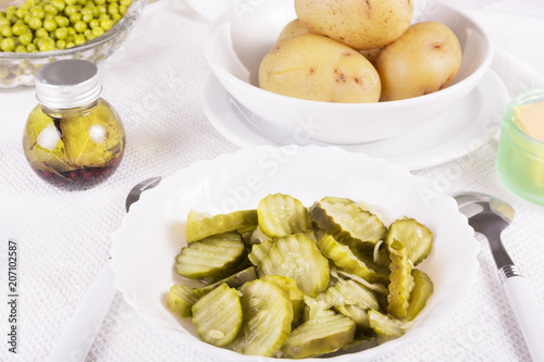 Healthy simple food - sliced gherkin pickles in a white bowl, boiled potatoes, green peas, oil and butter