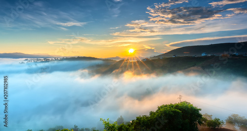 Dawn on plateau in morning with colorful sky, while sun rising from horizon shines down to small village covered with fog shrouded landscape so beautiful idyllic countryside Dalat plateau, Vietnam