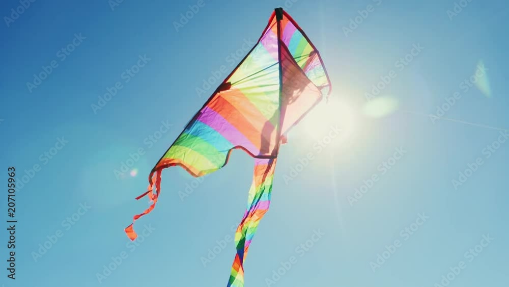 Rainbow hovering kite with a long tail against the background of the sun and blue sky in slow motion. Close-up