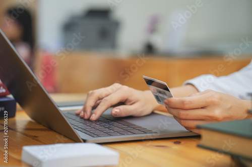 A woman's hand holds a credit card and uses a laptop computer to shop online.