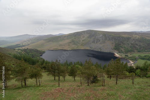Panoramic view of mountain range, green hills, vivid green color, mountain lake with black water in the foreground, summer, overcast day