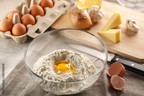 preparation of dough for flat bread. broken egg and flour in a glass bowl. flat bread with onion, cheese and garlic