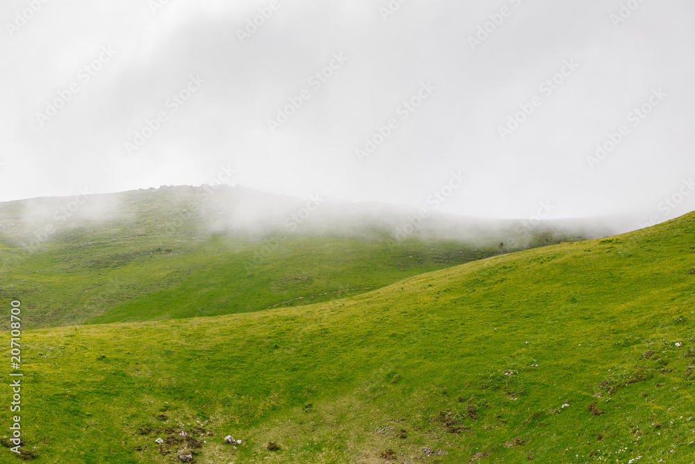 Beautiful mountain landscape with green hills on a cold foggy day, with sky and clouds