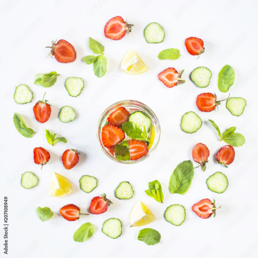 A glass of water with the addition of strawberries, cucumber, mint and lemon. In a circle of bright ingredients on a white background. Detox and Sports Concept. Top view, flat lay A glass of water with the addition of strawberries, cucumber, mint and lemon. In a circle of bright ingredients on a white background. Detox and Sports Concept. Top view, flat lay